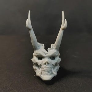 Op de afbeelding: Een gedetailleerde, grijze schedelsculptuur met prominente hoorns. De schedel heeft zichtbare tanden en oogkassen, met de hoorns die omhoog uitsteken. De sculptuur is waarschijnlijk een decoratief item of onderdeel van een grotere artistieke creatie.