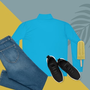 Peut inclure: Une tenue décontractée composée d'un haut turquoise à manches longues, d'un jean bleu et de chaussures de sport noires à semelles blanches. Une glace jaune ajoute une touche de couleur. Le fond est un mélange de jaune, de bleu et de gris.