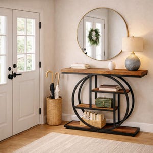 Puede incluir: Un recibidor moderno con un espejo redondo dorado y una consola de madera y metal negro. Una lámpara, objetos decorativos y un paragüero de mimbre también están presentes. El conjunto crea un ambiente acogedor.