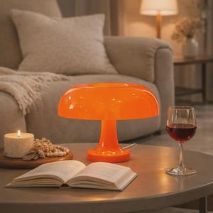 May include: An orange mushroom-shaped table lamp with a round base and a wide, curved shade. A lit candle, an open book, and a glass of red wine sit on a round table. A beige sofa is in the background.