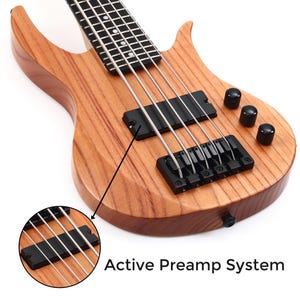 K&ouml;nnte beinhalten: Nahaufnahme einer Bassgitarre aus Holz mit nat&uuml;rlichem Finish. Das Instrument verf&uuml;gt &uuml;ber schwarze Hardware, einschlie&szlig;lich Steg, Tonabnehmern und Kn&ouml;pfen. Der Text "Active Preamp System" ist sichtbar.