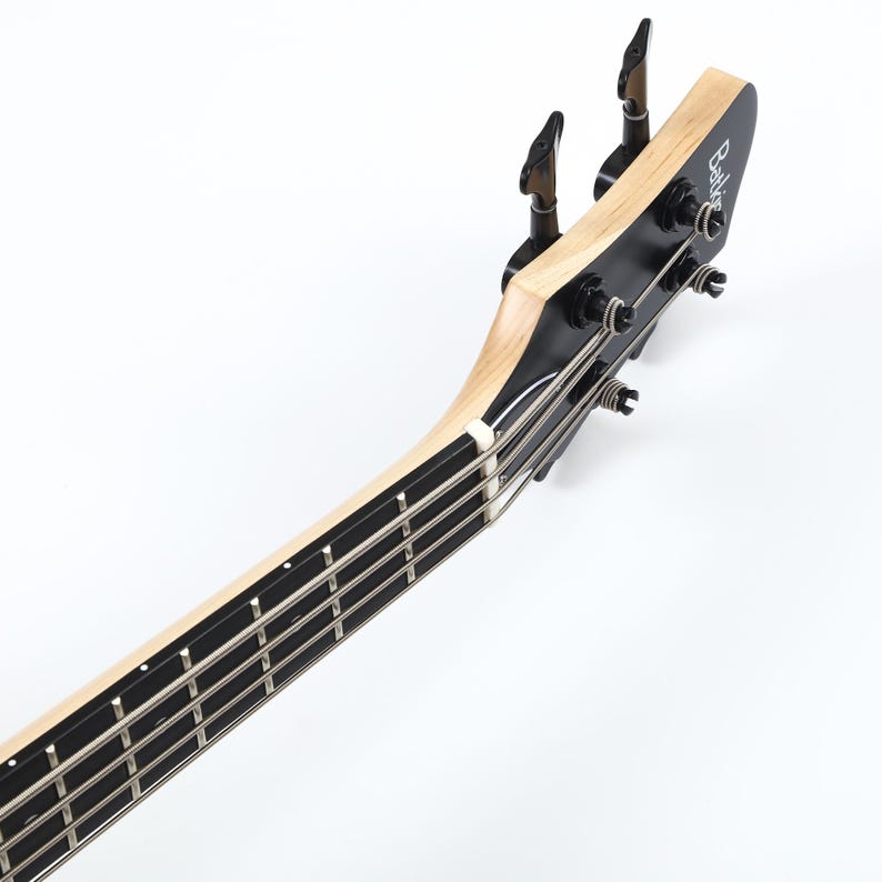 Peut inclure: Gros plan sur la t&ecirc;te et le manche d'une guitare basse noire et en bois naturel. La t&ecirc;te comporte des chevilles d'accord noires et le nom de la marque. Le manche a quatre cordes et des frettes noires. L'instrument est sur fond blanc.