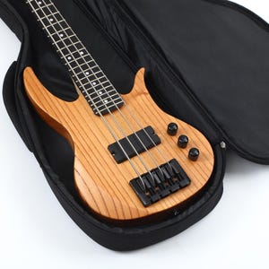 Peut inclure: Une guitare basse marron clair avec des &eacute;l&eacute;ments noirs est pr&eacute;sent&eacute;e dans un &eacute;tui de transport noir. Le corps en bois pr&eacute;sente un motif de grain naturel. La guitare a quatre cordes et trois boutons de contr&ocirc;le noirs.