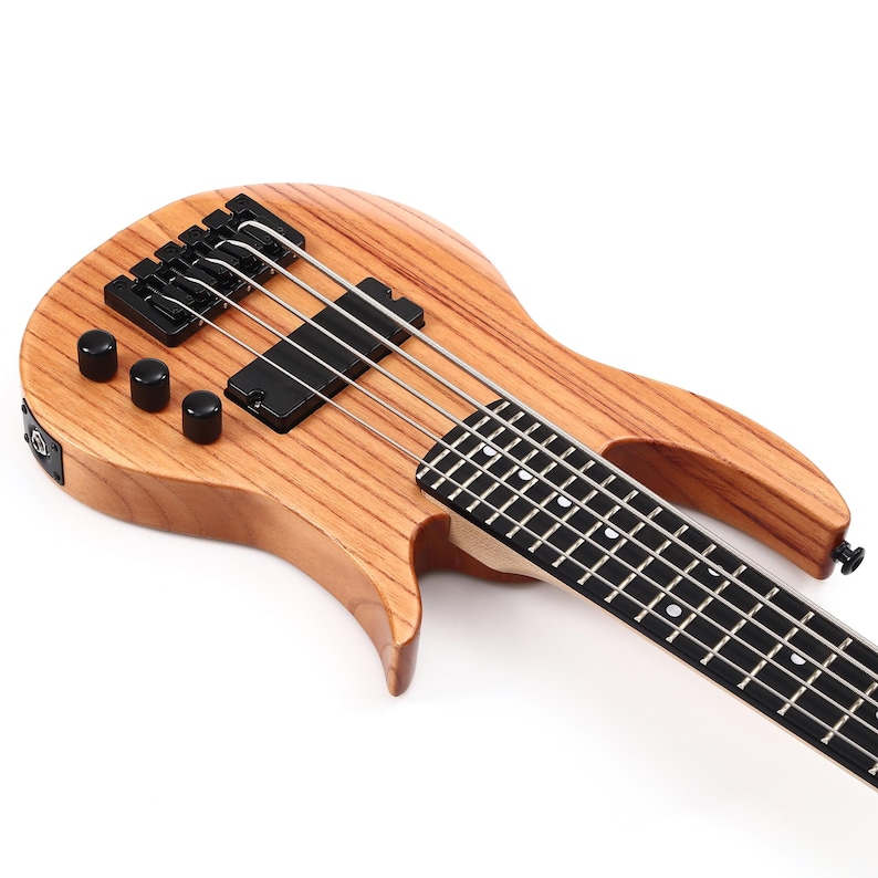 K&ouml;nnte beinhalten: Ein Bassgitarre aus Holz mit nat&uuml;rlichem Finish. Das Instrument hat vier Saiten, schwarze Stimmwirbel und einen schwarzen Tonabnehmer. Das Griffbrett ist schwarz mit wei&szlig;en Einlagen. Der Korpus hat eine geschwungene Form.