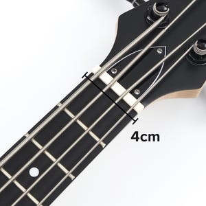 Peut inclure: Gros plan sur la t&ecirc;te et le manche d'une basse noire. Les cordes sont argent&eacute;es et la touche est noire. Le sillet est blanc et la distance est de 4 cm.