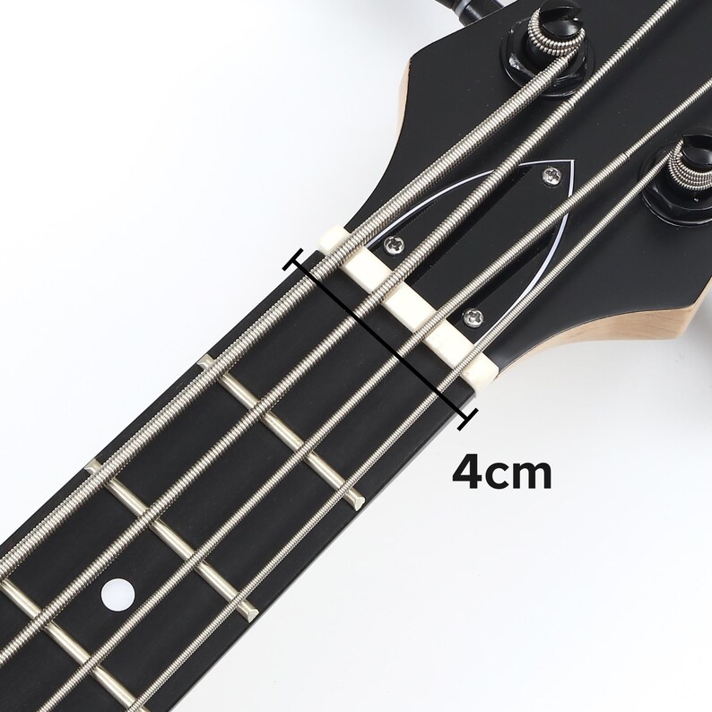 Peut inclure: Gros plan sur la t&ecirc;te et le manche d'une basse noire. Les cordes sont argent&eacute;es et la touche est noire. Le sillet est blanc et la distance est de 4 cm.