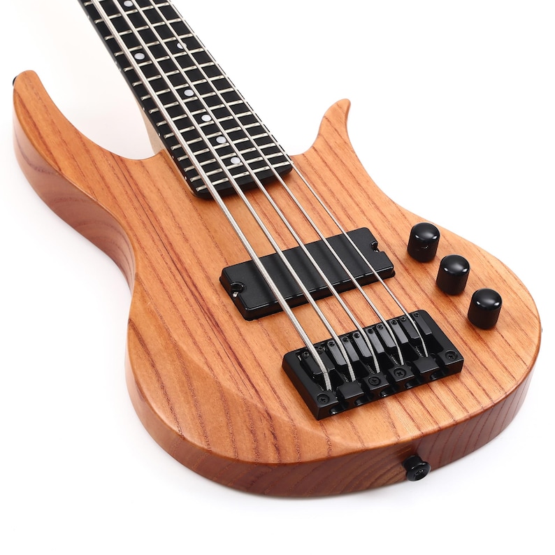 K&ouml;nnte beinhalten: Eine hellbraune Bassgitarre mit schwarzer Hardware, einschlie&szlig;lich Stimmkn&ouml;pfen, Tonabnehmern und einer Br&uuml;cke. Das Instrument hat vier Saiten und einen Holzk&ouml;rper mit sichtbarem Maserungsmuster. Das Griffbrett ist schwarz mit wei&szlig;en Einlagen.