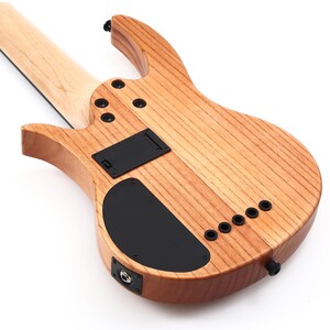 K&ouml;nnte beinhalten: Nahaufnahme der R&uuml;ckseite einer Bassgitarre aus Holz. Das Instrument hat eine hellbraune Holzmaserung mit schwarzer Hardware, einschlie&szlig;lich Batteriefach, Bedienfeld und Ausgangsbuchse. Der Hals ist aus hellerem Holz.