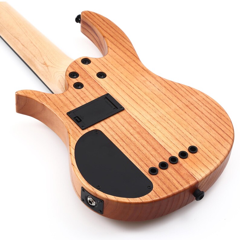 K&ouml;nnte beinhalten: Nahaufnahme der R&uuml;ckseite einer Bassgitarre aus Holz. Das Instrument hat eine hellbraune Holzmaserung mit schwarzer Hardware, einschlie&szlig;lich Batteriefach, Bedienfeld und Ausgangsbuchse. Der Hals ist aus hellerem Holz.