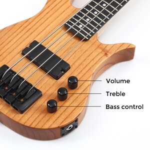 Peut inclure: Gros plan sur une guitare basse en bois avec des &eacute;l&eacute;ments noirs. La guitare comporte trois boutons de contr&ocirc;le noirs &eacute;tiquet&eacute;s "Volume", "Treble" et "Bass control". Les cordes sont argent&eacute;es et le corps a une finition en grain de bois naturel.