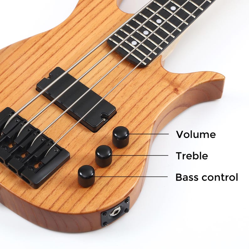 Peut inclure: Gros plan sur une guitare basse en bois avec des &eacute;l&eacute;ments noirs. La guitare comporte trois boutons de contr&ocirc;le noirs &eacute;tiquet&eacute;s "Volume", "Treble" et "Bass control". Les cordes sont argent&eacute;es et le corps a une finition en grain de bois naturel.