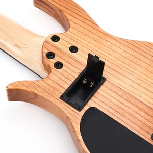 K&ouml;nnte beinhalten: Nahaufnahme der R&uuml;ckseite einer elektrischen Bassgitarre aus Holz. Der Korpus hat eine nat&uuml;rliche Holzmaserung mit schwarzer Hardware, einschlie&szlig;lich Schrauben und einem Batteriefach. Der Hals ist helles Holz.