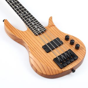 Peut inclure: Une guitare basse &eacute;lectrique marron clair avec un corps et un manche en bois. La basse a des micros, un chevalet et des boutons de r&eacute;glage noirs. Les cordes sont argent&eacute;es et la touche est noire avec des incrustations blanches. Le corps pr&eacute;sente un motif de grain de bois naturel.