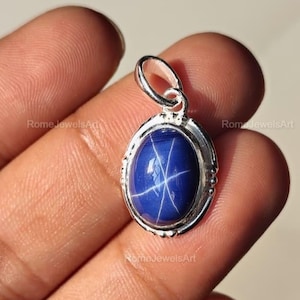 Puede incluir: Colgante ovalado con una vibrante piedra preciosa azul, que presenta un patrón en forma de estrella. El colgante está engastado en un marco de metal plateado. El color de la piedra es un azul profundo y saturado. Joyería.