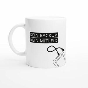 Könnte beinhalten: Ein weißer Keramikbecher mit einem schwarzen Grafikdesign, das den Text KEIN BACKUP KEIN MITLEID in zwei übereinanderliegenden rechteckigen Kästen zeigt, ergänzt durch eine einfache schwarze Strichzeichnung einer externen Festplatte mit USB-Kabel.