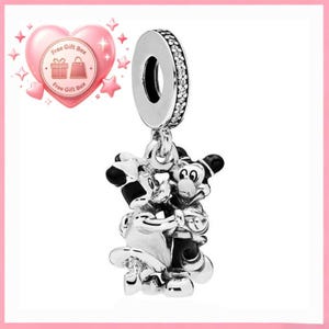 May include: A silver charm featuring Mickey and Minnie Mouse embracing. The charm has a circular top with a ring of small, clear stones. The figures are detailed with black and white accents.
