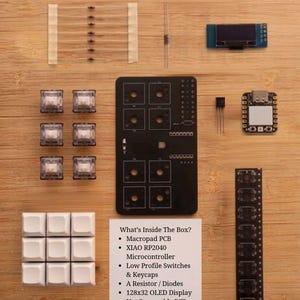 May include: A DIY Soldering Kit containing a black macropad PCB, a XIAO RP2040 microcontroller, six low-profile switches, nine white keycaps, a 128x32 OLED display, a resistor, diodes, hot-swappable PCB sockets, a transistor, and a haptic motor.