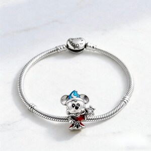 Puede incluir: Una pulsera de plata con un charm de Mickey Mouse. El charm de Mickey Mouse lleva un sombrero de mago azul y una t&uacute;nica roja, sosteniendo una varita en forma de estrella. La pulsera es de plata y tiene un cierre.