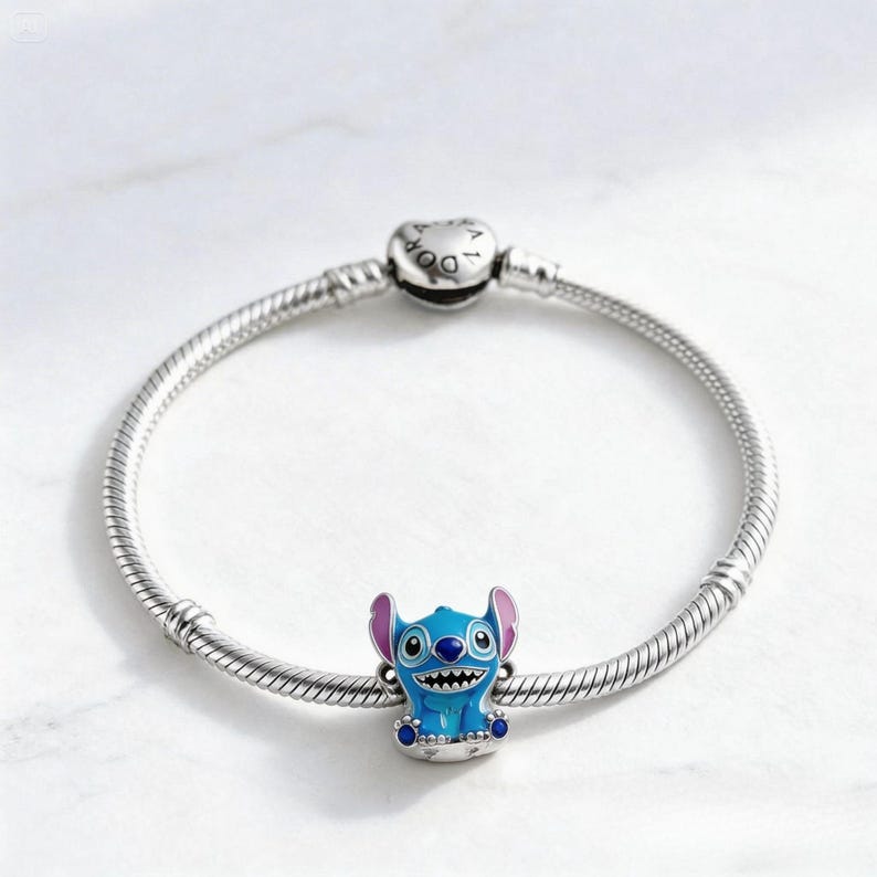 May include: A silver charm bracelet with a blue, pink, and white Stitch charm. The charm features Stitch, a character from the animated film Lilo & Stitch. The bracelet has a round clasp with the word "Pandora" on it.