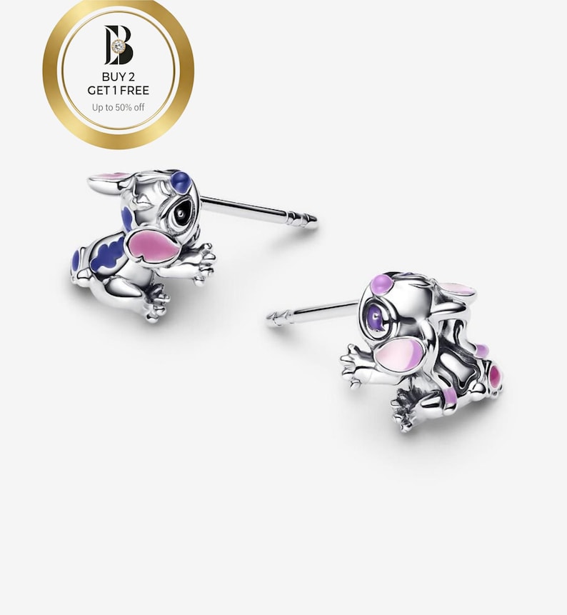 May include: A pair of silver-colored stud earrings featuring a cartoon character design. The earrings have blue and pink accents. The image also includes a gold-colored circle with text that reads "BUY 2 GET 1 FREE Up to 50% off."