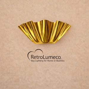 Könnte beinhalten: Eine goldfarbene Wandleuchte mit gewelltem Rand. Die Leuchte hat eine reflektierende, metallische Oberfläche und ist auf einem neutralfarbenen Hintergrund montiert. Der Text "RetroLumeco. Buy Lighting for Home or Business" steht darunter.