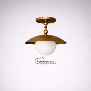 Könnte beinhalten: Eine messingfarbene Deckenleuchte mit einem weißen, kugelförmigen Schirm. Die Leuchte hat einen kreisförmigen Sockel und einen geschwungenen, schalenförmigen Schirm. Der Text "RetroLumeCo. Buy Lighting for Home or Business" steht unten.