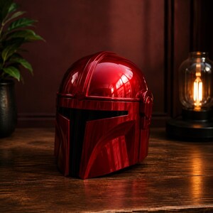 May include: A glossy, metallic red helmet featuring a T-shaped visor design with a black faceplate. The helmet has a smooth, rounded dome and a structured, angular front section, reflecting light across its polished, vibrant crimson surface.