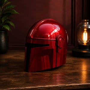 May include: A glossy, metallic red helmet featuring a T-shaped visor opening, a smooth rounded dome, and raised side ear-cap details. The helmet has a reflective surface that catches light, showcasing its curved, aerodynamic design and solid construction.