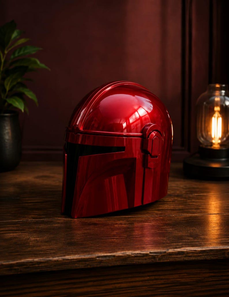 May include: A glossy, metallic red helmet featuring a T-shaped visor opening, a smooth rounded dome, and raised side ear-cap details. The helmet has a reflective surface that catches light, showcasing its curved, aerodynamic design and solid construction.