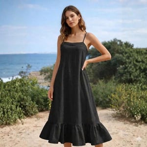 Puede incluir: Un vestido negro liso de largo midi con tirantes finos, escote recto y un dobladillo con volantes. La prenda tiene una silueta relajada y fluida que cae por debajo de las rodillas, confeccionada con una tela sencilla de color oscuro.