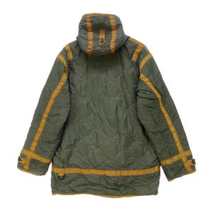 Op de afbeelding: Olijfgroene gewatteerde jas met capuchon en goudkleurige accenten. De jas heeft gouden strepen langs de mouwen en rond de onderkant. De jas heeft een gewatteerd patroon en een D-ring detail.