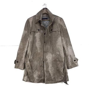 May include: A tan trench coat with a textured pattern, button fastenings, and a belt. The coat has a classic design with a collared neckline and long sleeves. The coat is hanging on a wooden hanger.