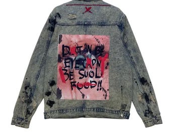 May include: Acid wash denim jacket with paint splatter details and distressed accents. The back features a pink and red graphic with the text "D.T.N.B. EYE CAPN BE SUOL FOOD!!" and a red "X" on the upper back.