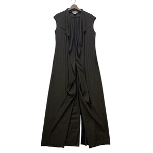 May include: A sleeveless, floor-length dark gray vest with a cascading ruffle detail down the front. The vest is hanging on a wooden hanger against a white background. The garment has a split front design.