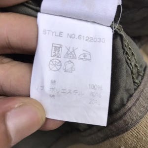 Puede incluir: Una etiqueta de ropa blanca con el texto "STYLE NO.6122030" y varios s&iacute;mbolos de cuidado. La etiqueta tambi&eacute;n enumera la composici&oacute;n de la tela: 100% algod&oacute;n, 80% poli&eacute;ster y 20% otros.