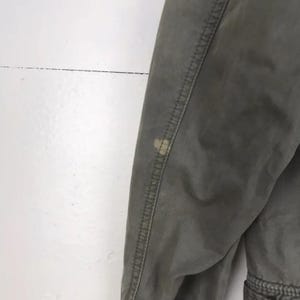 Puede incluir: Primer plano de un pantal&oacute;n verde oliva con costuras visibles y una mancha de color claro en la tela. El pantal&oacute;n parece estar hecho de un material duradero, con un enfoque en la textura y los detalles de la prenda.