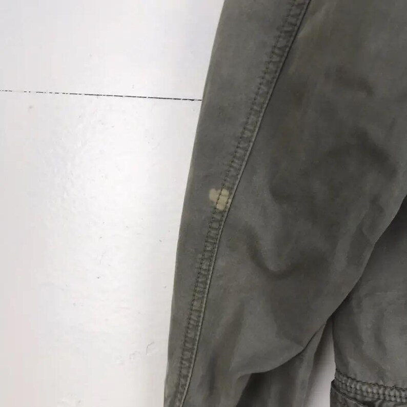 Puede incluir: Primer plano de un pantal&oacute;n verde oliva con costuras visibles y una mancha de color claro en la tela. El pantal&oacute;n parece estar hecho de un material duradero, con un enfoque en la textura y los detalles de la prenda.