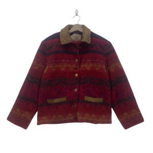 May include: A red, patterned jacket with a brown suede collar and pocket accents. The jacket has a button-up front and is hanging on a hanger. The pattern includes black and gold geometric shapes.