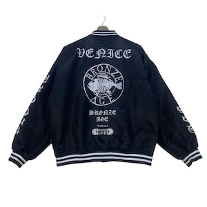 May include: Black bomber jacket with white trim and lettering. The back features a circular graphic with a fish skeleton and the words "VENICE BRONZE AGE". The sleeves have white lettering. A classic streetwear style.