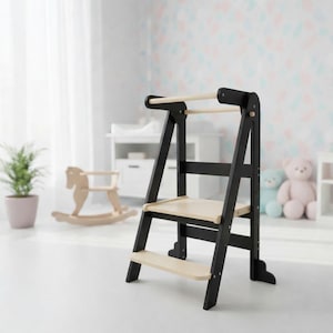 May include: A black and natural wood step stool with two steps and a safety bar. The stool is designed for children and has a sturdy A-frame construction. The steps and bar are made of light-colored wood, while the frame is black.