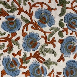 May include: Close-up of a fabric with a repeating floral pattern. The design features light blue flowers with orange and green accents on a white background. The flowers are surrounded by orange vines and green leaves.