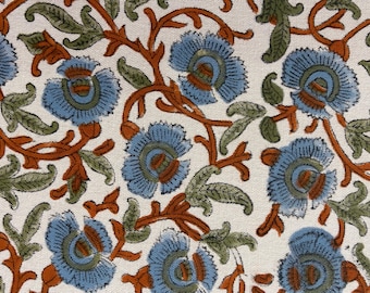 May include: Close-up of a fabric with a repeating floral pattern. The design features light blue flowers with orange and green accents on a white background. The flowers are surrounded by orange vines and green leaves.