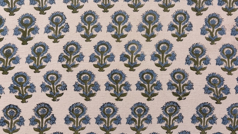 May include: Close-up of a fabric with a repeating floral pattern. The design features blue flowers with green stems and leaves on a cream-colored background. The fabric has a textured appearance.