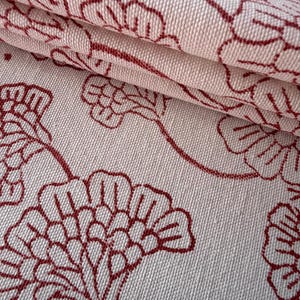 Könnte beinhalten: Nahaufnahme eines gefalteten Stoffes mit einem sich wiederholenden Blumenmuster. Die Blumen sind tiefrot und auf einem hellbeigen Hintergrund umrandet. Der Stoff hat ein strukturiertes Aussehen.