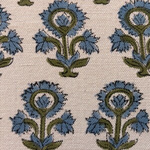 May include: Close-up of a fabric with a repeating floral pattern. The design features stylized blue flowers with green stems and leaves against a cream-colored background. The fabric has a textured appearance.