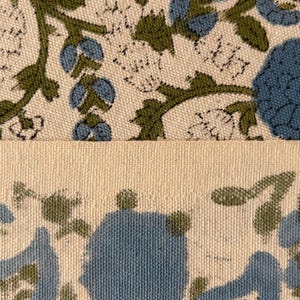May include: Close-up of two sections of fabric. The top section features a floral pattern with blue flowers and green leaves on a cream background. The bottom section is a solid cream color with a floral pattern along the bottom edge.