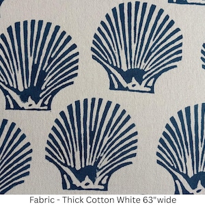 May include: A thick white cotton fabric featuring a repeating pattern of dark blue seashell illustrations. The textile is 63 inches wide and displays a consistent print of fan-shaped shells arranged in a grid across the surface of the material.