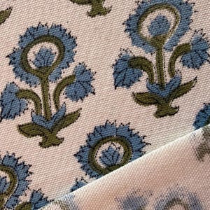 May include: Close-up of a fabric with a repeating floral pattern. The flowers are blue with green stems and leaves, set against a cream-colored background. The fabric is folded over, revealing the pattern on both sides.