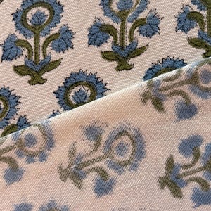 May include: Close-up of two pieces of fabric with a floral pattern. The design features blue flowers with green stems and leaves on a cream background. The fabric has a textured appearance.