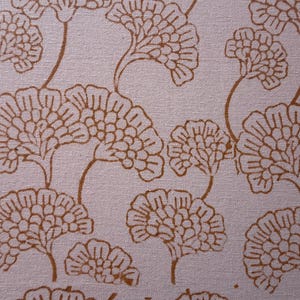 May include: Close-up of a fabric with a repeating pattern of stylized, brown floral shapes on a light pink background. The design features detailed outlines of the flowers and stems, creating a textured appearance.